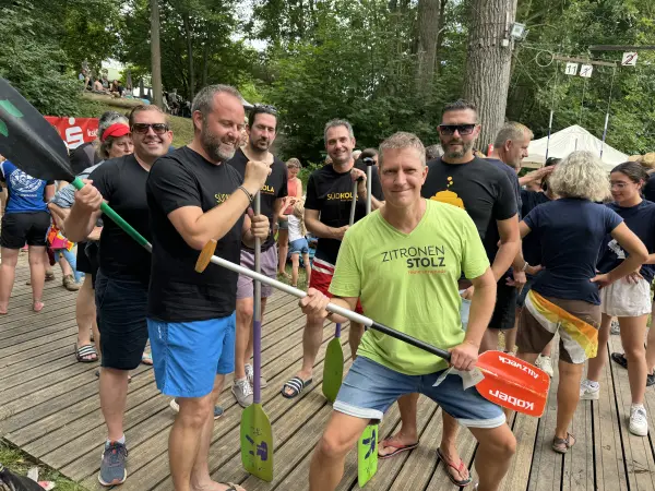 Das SÜDKOLA-Männerteam jubelt mit Paddeln auf dem Steg, einer im grünen ZITRONENSTOLZ-Shirt