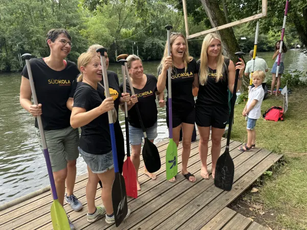 Das SÜDKOLA-Frauenteam mit Paddeln am Steg, alle in schwarzen SÜDKOLA-Shirts
