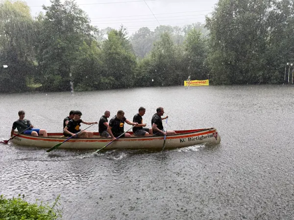 Sechs Paddler in schwarzen Shirts ziehen durch den Regen, die Wasseroberfläche voller Tropfen